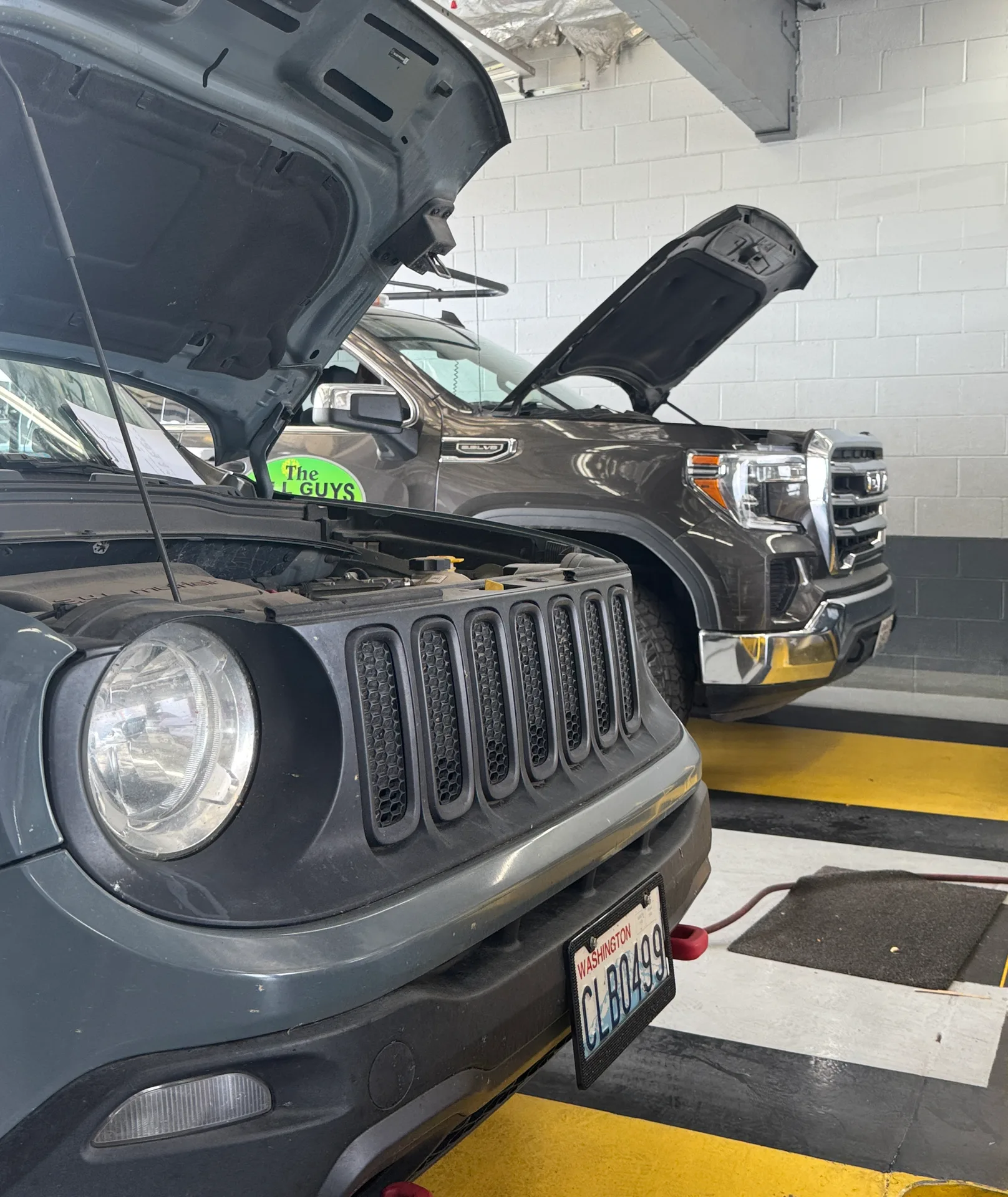 Two vehicles in the service bay with hoods up
